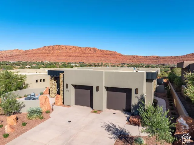 Modern stucco exterior featuring dual garage bays, stone masonry accents, desert landscaping, and a mountain backdrop