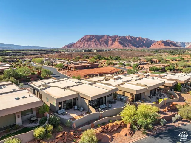 Aerial perspective featuring flat-roof desert architecture, concrete patios, integrated outdoor kitchen stations, stucco perimeter walls, and red rock mountain scenery