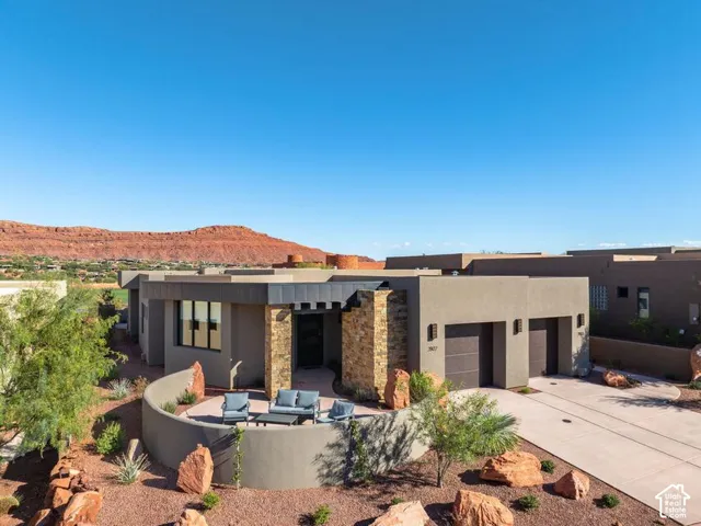 Contemporary exterior featuring a textured stone facade, integrated multi-car garage, curved stucco privacy wall, and desert-inspired landscaping against a mountain backdrop