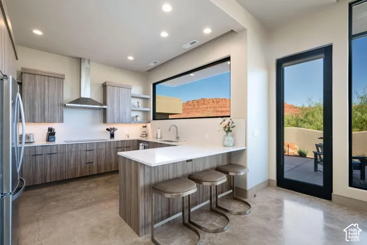 Kitchen featuring wood-finish cabinetry, stone-surface countertops, stainless steel range hood, recessed lighting, and concrete flooring