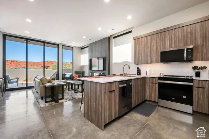 Kitchen featuring wood-finish cabinetry, stone-surface countertops, stainless steel appliances, polished concrete flooring, and full-height sliding glass doors