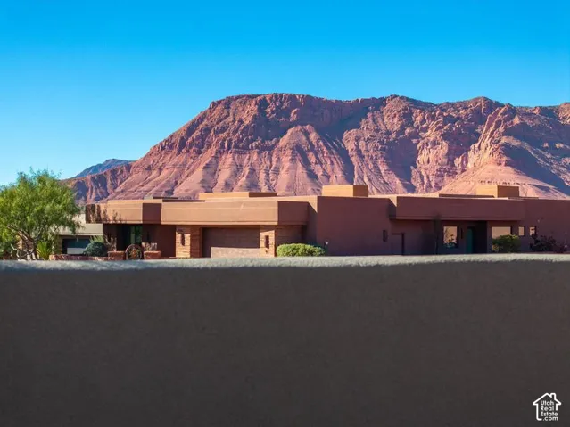 Single-story residence featuring a smooth stucco exterior, attached garage, stone accents, and red rock mountain scenery