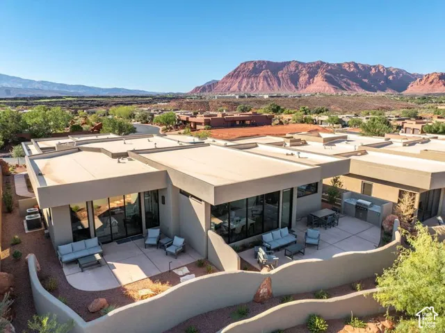 Contemporary residence featuring an expansive concrete patio, built-in outdoor kitchen, floor-to-ceiling glass wall systems, and prominent mountain backdrop