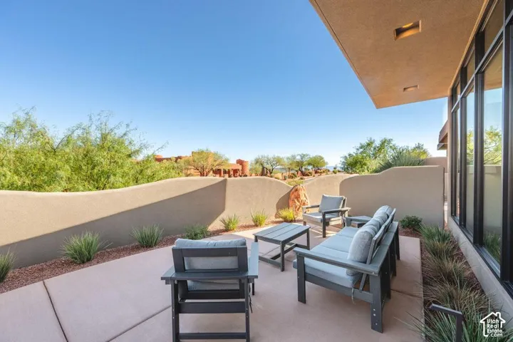 Covered concrete patio featuring a serpentine stucco privacy wall, desert landscaping, and full-height glass windows