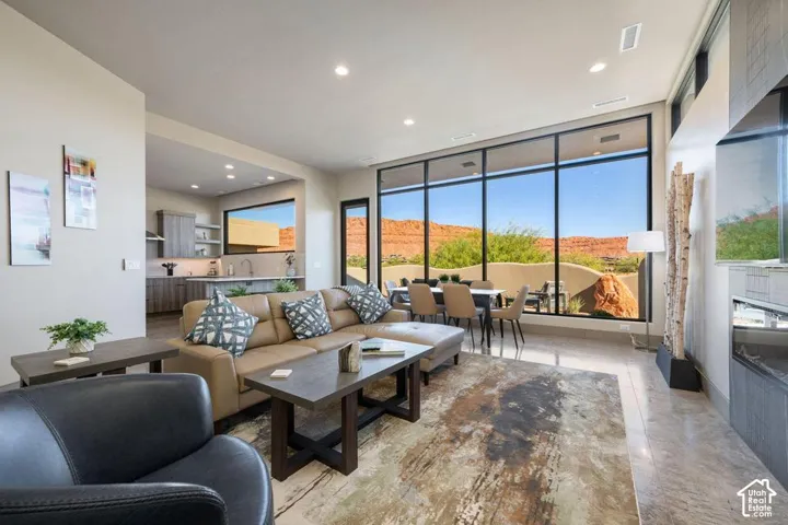 Open-concept interior featuring floor-to-ceiling windows, polished tile flooring, a horizontal linear fireplace with stacked stone surround, and wood-finish cabinetry