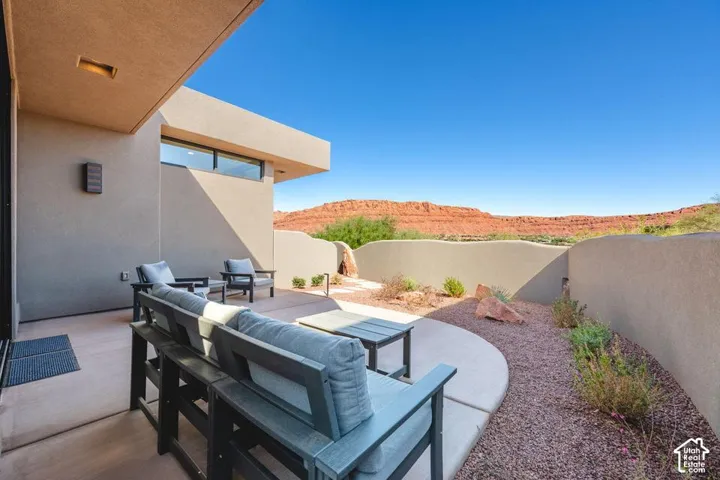 Covered concrete patio featuring a stucco privacy wall, desert landscaping, and prominent red rock scenery