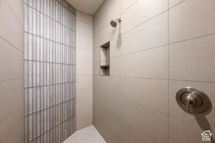 Walk-in shower featuring large-format neutral wall tile, a vertical textured accent tile inlay, a built-in recessed shelf, and brushed nickel hardware