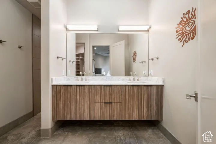 Floating dual-sink vanity featuring wood-finish cabinetry, stone countertop, integrated lighting, and wall-mounted faucets over large-format tile flooring