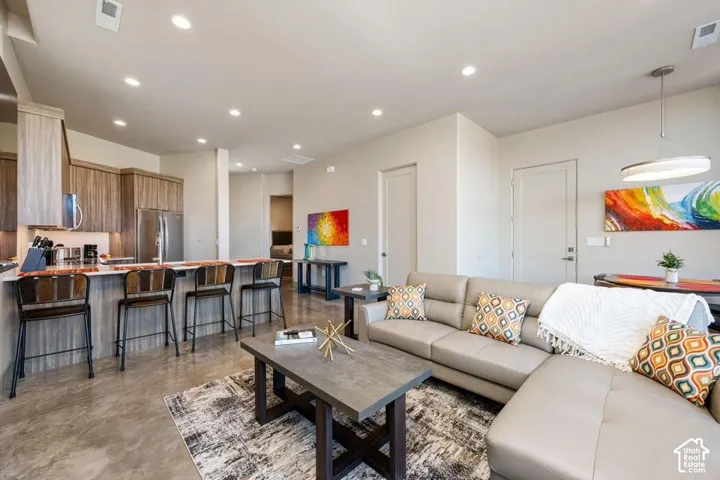 Kitchen featuring wood-finish cabinetry, stainless steel appliances, and a breakfast bar with stone-surface countertop, complemented by recessed lighting and concrete flooring throughout the space