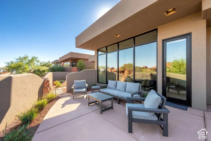 Concrete patio featuring a stucco privacy wall, floor-to-ceiling windows with black frames, and recessed lighting