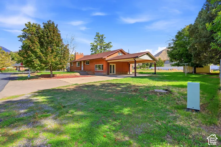 Single-story brick exterior featuring a covered carport, masonry chimney, and mountain backdrop