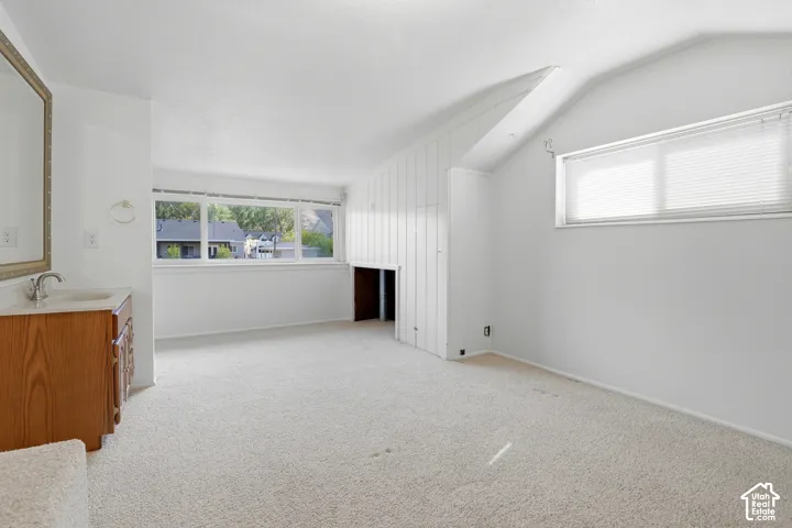 Sloped ceilings featuring vertical wood paneling, wall-to-wall carpeting, wood-finish vanity, and large windows with horizontal blinds