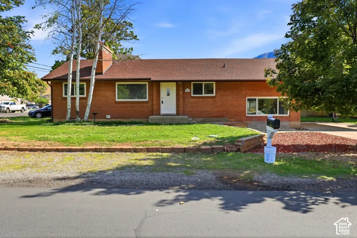 Single-story brick exterior featuring a multi-pitched asphalt shingle roof, a central chimney, horizontal windows, and an elevated concrete front porch