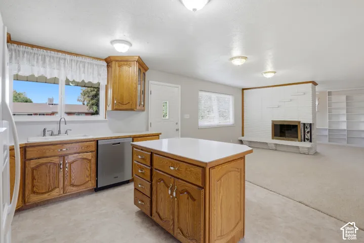 Kitchen featuring medium-tone wood cabinetry, a center island with a solid surface countertop, stainless steel dishwasher, and white brick fireplace with built-in shelving
