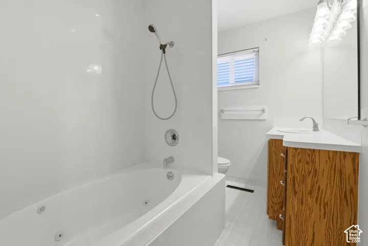 Bathroom featuring a jetted soaking tub, white surround, vanity with wood cabinetry, integrated sink, and multi-bulb light fixture