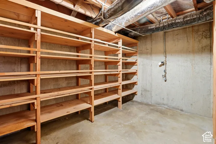 Storage area featuring built-in wood shelving units, concrete walls, and concrete flooring