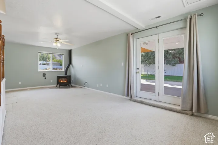 Living area featuring carpeted flooring, a freestanding wood-burning stove, a ceiling fan with integrated lighting, and glass double doors