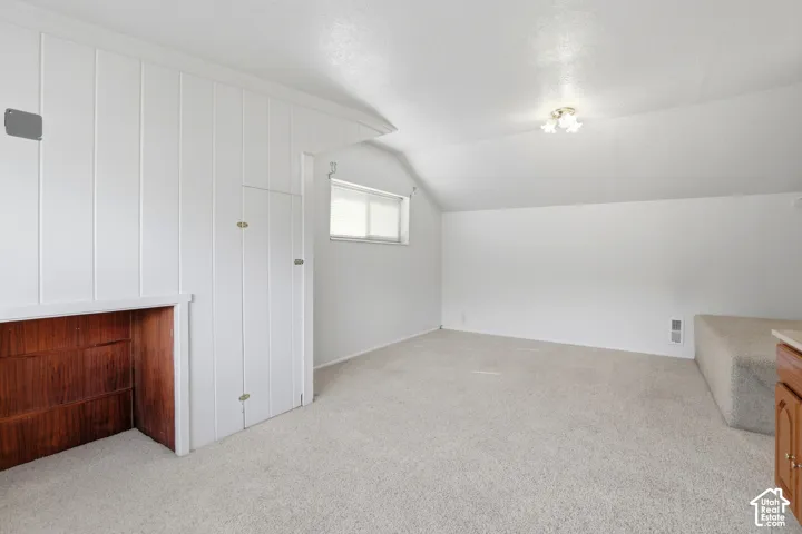 Vertical wood-paneled accent wall, neutral carpeting, sloped ceilings, and built-in wood cabinetry