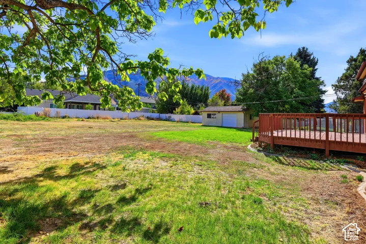 Expansive backyard featuring a raised wooden deck, detached garage, white vinyl fencing, and mountain scenery