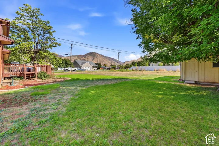 Expansive backyard featuring a lawn area, mature trees, an elevated wood deck, a detached storage shed, and a mountain backdrop