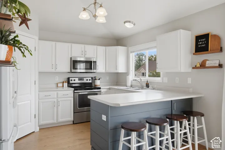 Kitchen featuring white shaker-style cabinetry, a peninsula with shiplap detailing, stainless steel appliances, light-toned wood-finish flooring, and a window above the sink