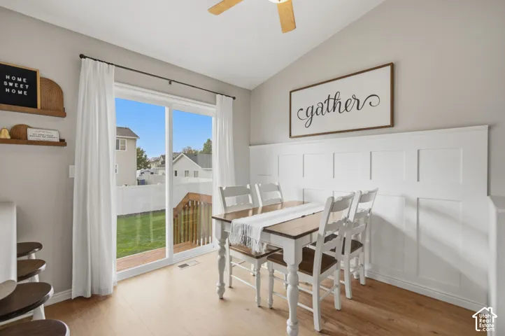 Vaulted ceiling with integrated ceiling fan, white grid wainscoting, wood-finish flooring, and sliding glass door with external deck access