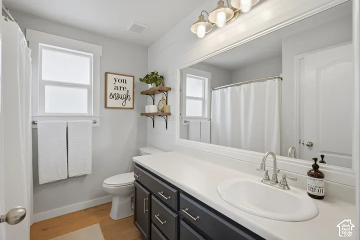 Bathroom featuring white horizontal plank wall detailing, charcoal gray vanity cabinetry, a solid-surface countertop with an integrated basin, a large framed vanity mirror, and wall-mounted three-light fixture