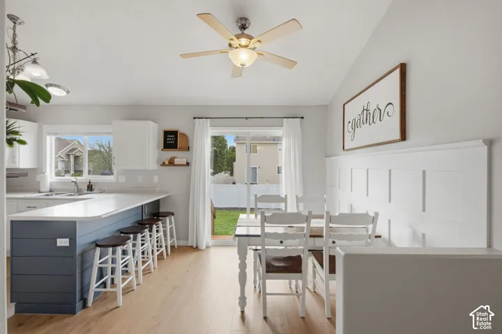 Kitchen island with horizontal shiplap base, wood-finish flooring, white board-and-batten wall detailing, ceiling-mounted paddle fan with integrated lighting, and sliding glass door
