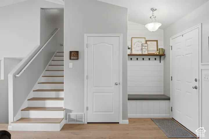Foyer featuring wood-finish flooring, a built-in bench with shiplap backing and wall-mounted hooks, a wood-tread staircase with a metal handrail, and a pendant light fixture