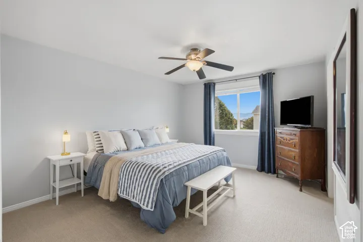 Neutral-toned carpeted flooring, window with natural lighting, and a multi-blade ceiling fan with integrated lighting