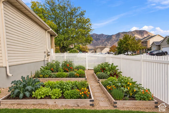 Side yard featuring three raised garden beds, wood-frame borders, gravel ground cover, and a white vinyl fence, complemented by a mountain backdrop
