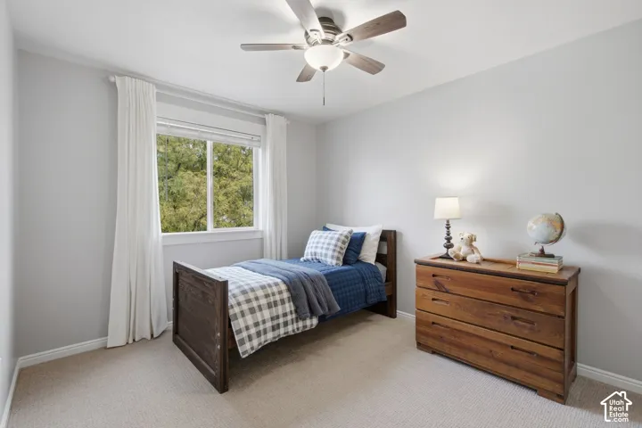 Neutral-toned wall paint, neutral carpeting, window with outdoor scenery, and a ceiling fan with integrated lighting