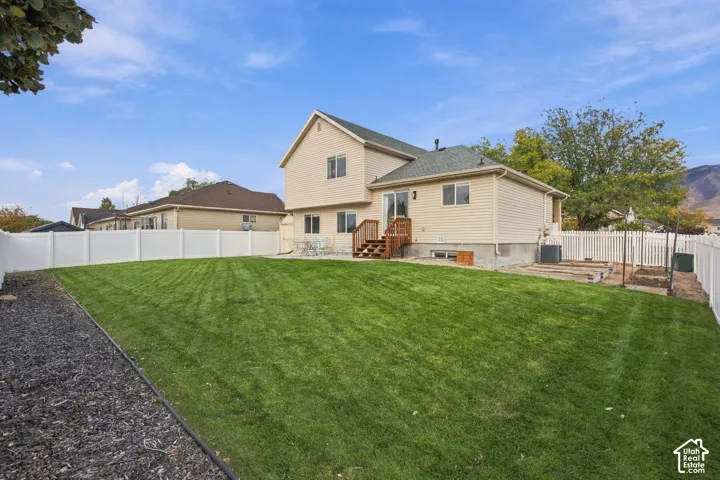 Backyard featuring a manicured lawn, white vinyl fencing, a raised wood deck, and designated garden beds