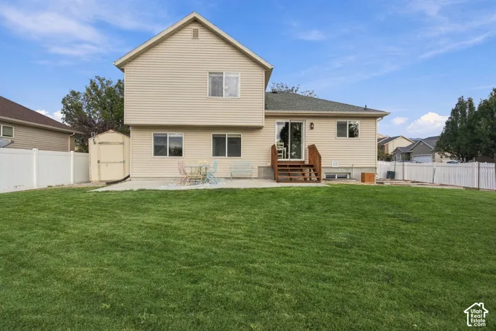 Rear exterior featuring light-colored horizontal siding, a concrete patio, a wood-framed staircase, a detached storage shed, and a full-perimeter privacy fence