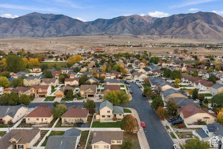 Aerial view of a residential neighborhood featuring multi-story dwellings, paved roadways, established tree growth, and a prominent mountain range backdrop