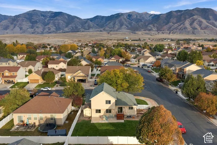 Aerial perspective showcasing a residential property with a paved patio, fenced backyard, mature trees, and prominent mountain backdrop