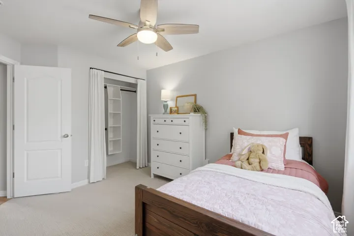 Bedroom featuring neutral-toned carpeting, a multi-blade ceiling fan with integrated lighting, and a closet with built-in shelving