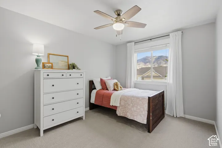 Bedroom featuring neutral-toned carpeting, a ceiling fan with integrated lighting, and a large window showcasing mountain scenery