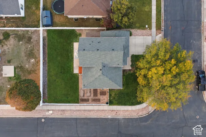 Aerial perspective featuring a corner lot, a concrete driveway, a fenced backyard with a grass lawn, and a dedicated garden area