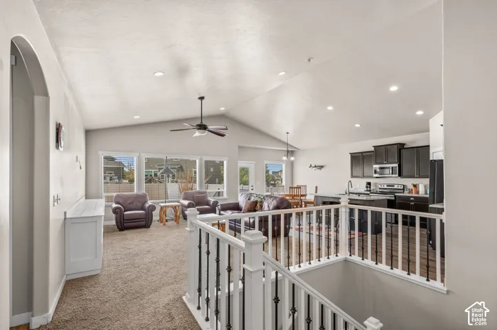 Vaulted ceilings, recessed lighting, white railing with iron balusters, dark-toned cabinetry, and a kitchen island