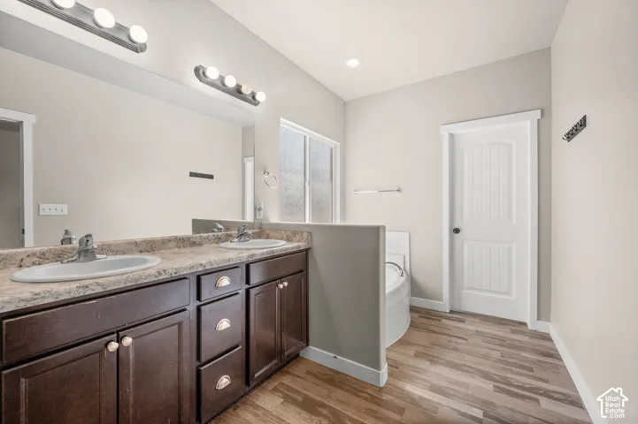 Double-sink vanity with stone-finish countertop, dark wood cabinetry, wood-finish flooring, and wall-mounted vanity lighting