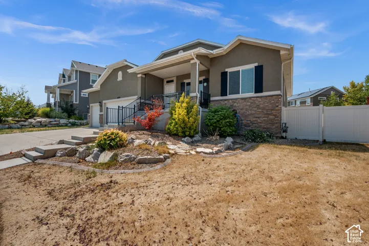 Exterior featuring a mixed-material facade of stucco and stone veneer, a covered front entryway, dark decorative shutters, and metal railing accents