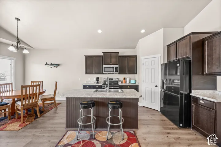 Kitchen featuring dark wood cabinetry, center island with stone-finish countertop, stainless steel sink, built-in microwave, and wood-finish flooring