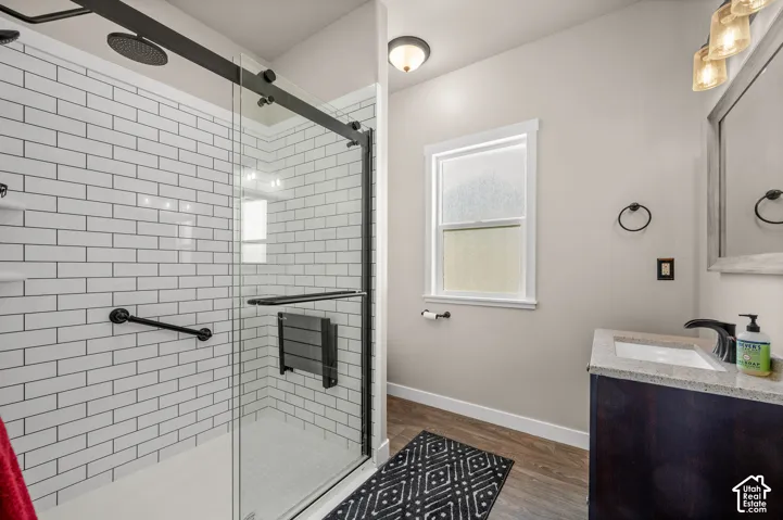 Walk-in shower with white subway tile, glass sliding doors, and matte black hardware, paired with a dark wood-finish vanity featuring a stone-composite countertop and wall-mounted light fixtures