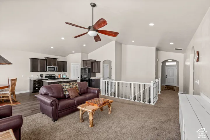 Vaulted ceilings, recessed lighting, ceiling fan with wood-finish blades, cabinetry with integrated appliances, and a staircase railing featuring metal balusters