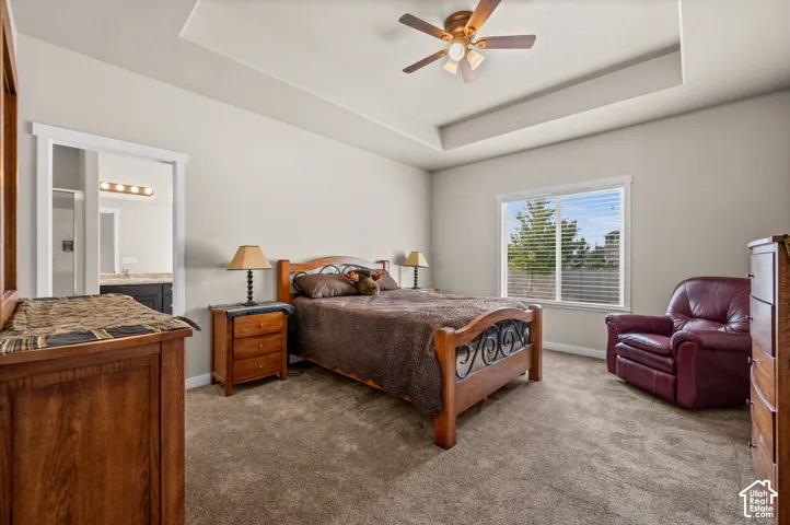Spacious bedroom featuring a tray ceiling, neutral wall tones, wall-to-wall carpeting, and a ceiling fan with integrated lighting