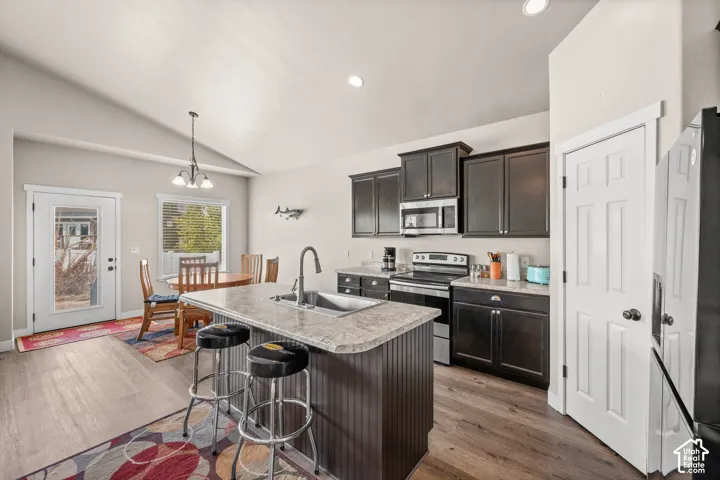 Kitchen featuring a center island with a stainless steel sink, dark wood cabinetry, laminate countertops, wood-finish flooring, and vaulted ceilings