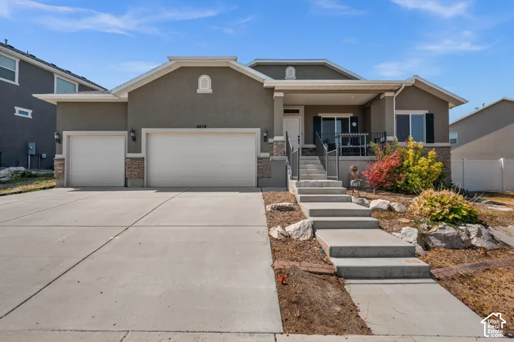 Stucco exterior featuring stone masonry accents, a three-car garage, and concrete walkway with steps leading to a covered entryway