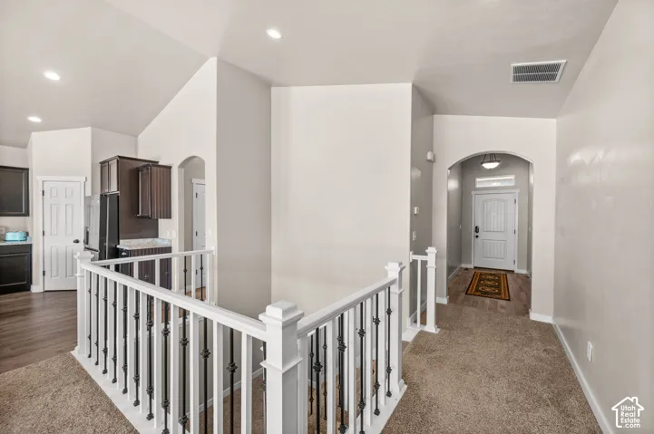 Vaulted ceilings, white-painted railing with metal balusters, arched architectural openings, recessed lighting, and wall-to-wall carpet