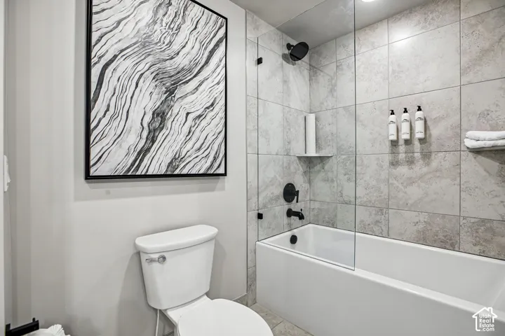 Bathroom featuring large-format neutral tile wall surround, frameless glass shower panel, matte black shower fixtures, and built-in corner shelving